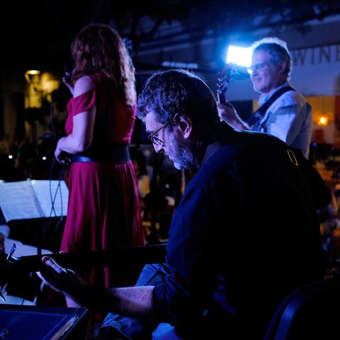 A bassist is playing, and in the background you see a guitarrist and a singer