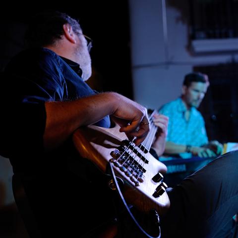 Lateral view from a bassist playing on stage. In the background there is a pianist also playing.