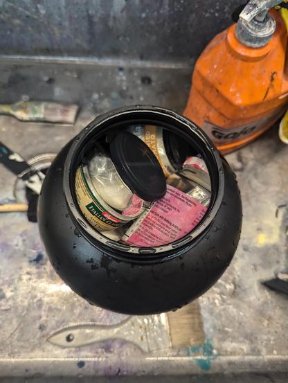 bunch of food jars with cotton balls in them submerged in water in a large black jug in a dirty slop sink.