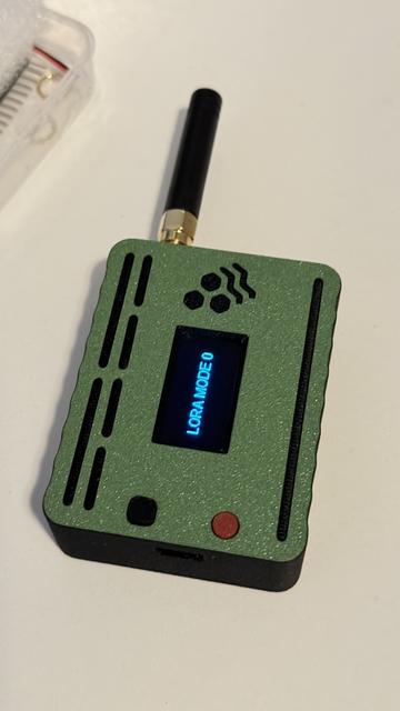 A new case for the Heltec V3. This case has a top-mounted antenna, which makes it easier to use larger antennas. The OLED screen shows "LORA MODE 0" which is the default unflashed message of a Heltec LoRa board without Meshtastic installed.