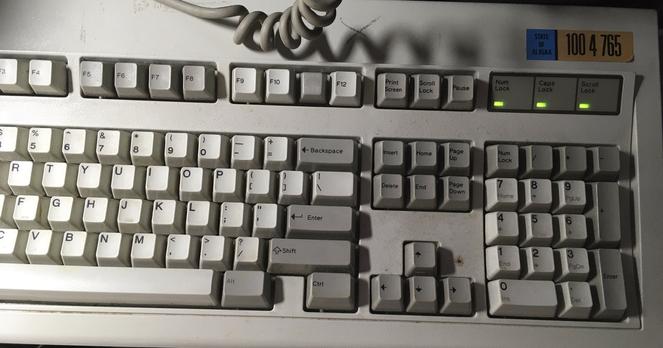 Photo of the right side of an IBM Model M keyboard with all three lock LEDs illuminated. You can see the curly keyboard cable at the top.