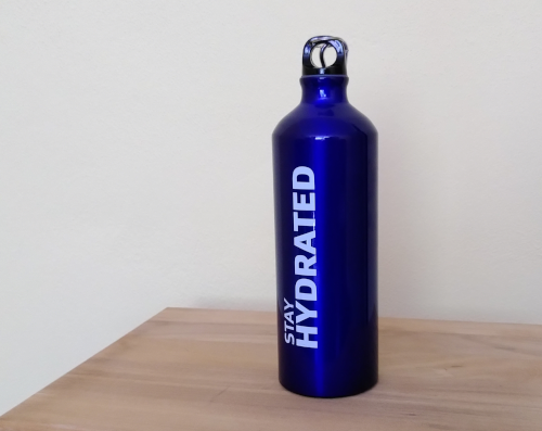 Eine blaue Stahltrinkflasche auf einem Holztisch. Auf der Flasche steht in weißer Schrift "stay hydrated"