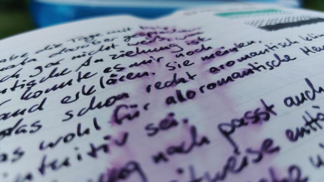 Close up photo at a shallow angle of my diary. The dark purple ink has been partly washed away but the text hasn't lost any of its readability because the dark grey part of the ink didn't go anywhere. However, you cannot read much of the text because the photo doesn't show the whole width of the page and only part of it is in focus.