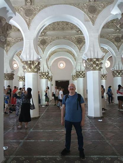 Mudéjar-style interior architecture, with ornate arches and pillars, in a synagogue built around the year 1200. Modern tourists explore the building.