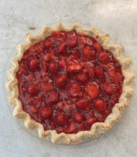 Bright red 9 inch strawberry pie with fluted edges on the crust, sitting on a stone counter