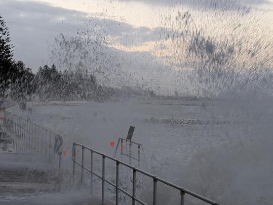 High tide big swells washing up on the beach and foreshore walls and railing
