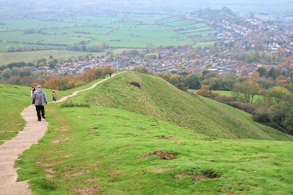 A long path, made from low steps, running along the top of  a grass-covered hill and disappearing at the end.
Below/in the background is a town with lots of black roof. Beyond, slightly misty, are paddocks, divided by hedges,