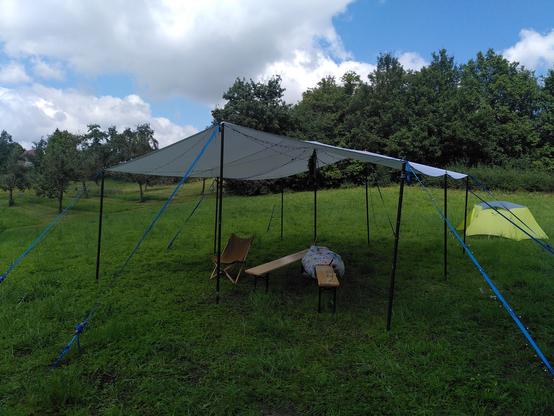 A big white tarp on a green field.
Underneath there are a chair and two benches.
