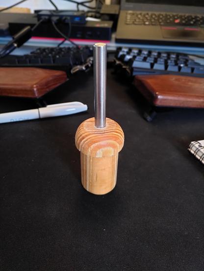 A round piece of wood with a small lip on the top and a stainless steel pin in the top.