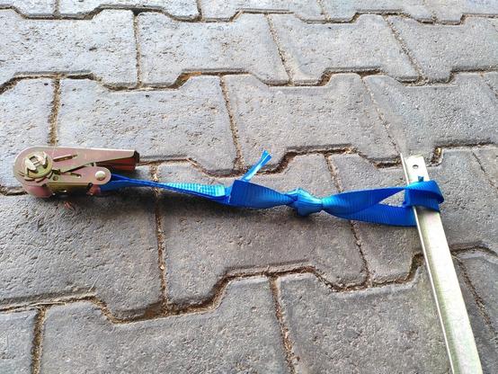 a blue ratchet strap wrapped around a T shaped tent peg.