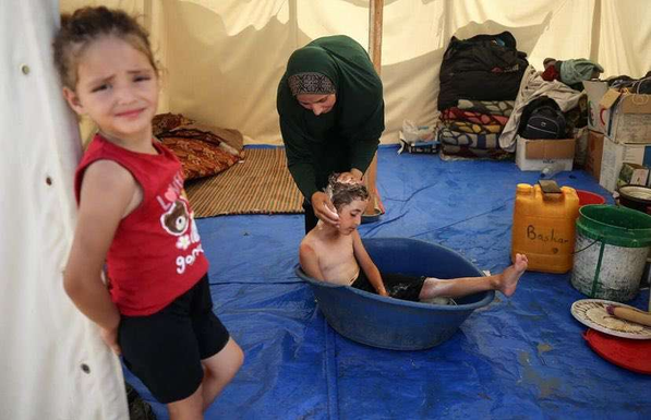 Una madre palestinese fa il bagno al suo bambino in una tenda improvvisata nella Striscia di Gaza (social media)