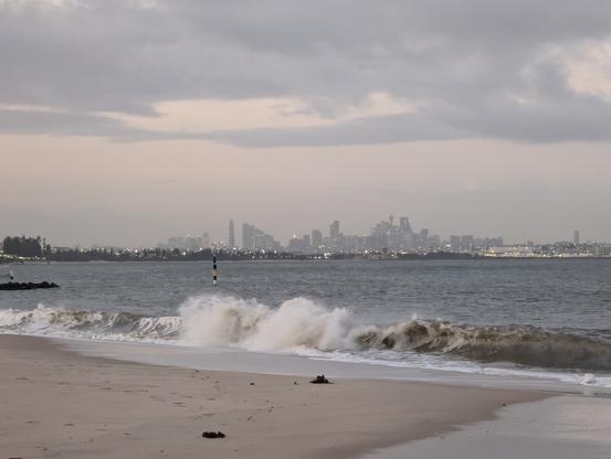 Sydney metropolitan skyline seen across the bay harbour with high tide swells hammering the foreshore beach