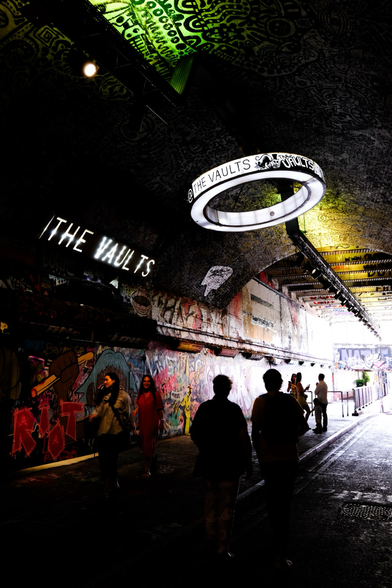 A shot from within the Leake street graffiti tunnel to the end. On the wall end the ceiling are sign which say “the vault” and people are walking in and out of the tunnel