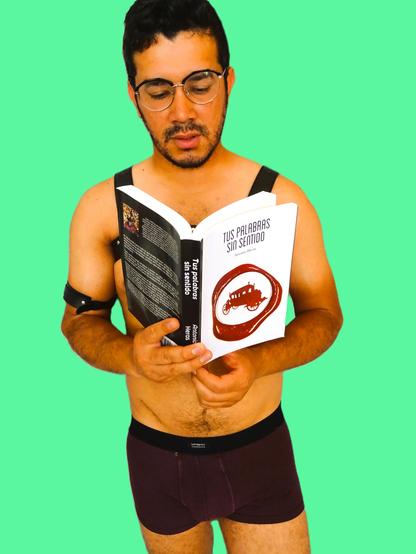 atractivo joven leyendo con gafas un libro, viste arnés y boxer granate.