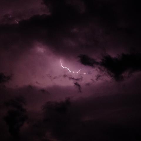 A dramatic image of lightning flashing across a dark, cloudy night sky, with purple hues illuminating the clouds, capturing the intensity and beauty of a thunderstorm.