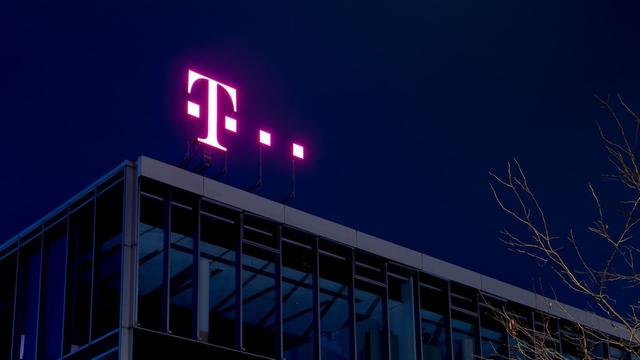 Leuchtendes „T“ der Deutschen Telekom auf einem Gebäudedach bei Nacht.