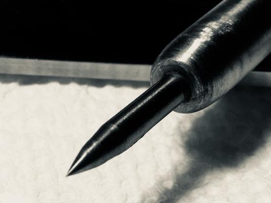 Broken 1/8” carbide grinding bit sharpened to a point at one end and fitted into a 3/8” diameter steel shaft. Closeup of sharp carbide scribing and punching point where it leaves chamfered 3/8” diameter handle.