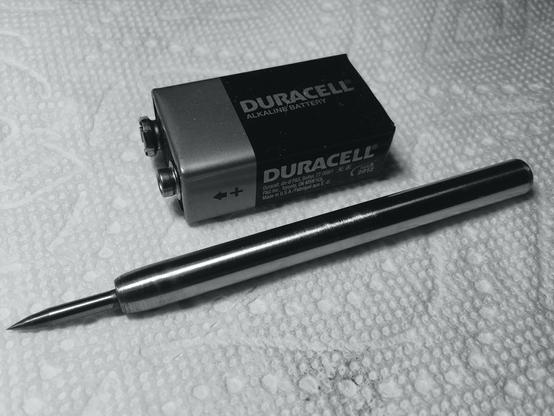 Broken 1/8” carbide grinding bit sharpened to a point at one end and fitted into a 3/8“ diameter steel shaft. Total length about three 9 volt batteries in length. Nine volt battery at top foot scale.