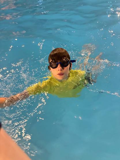 Child wearing goggles and a yellow swim shirt in a pool