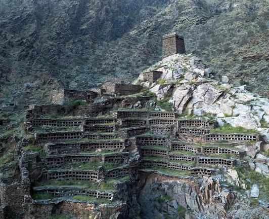 Struttura in pietra dai numerosi fori paralleli, scolpita nel versante di una montagna e sormontata da una torre di guardia medievale.