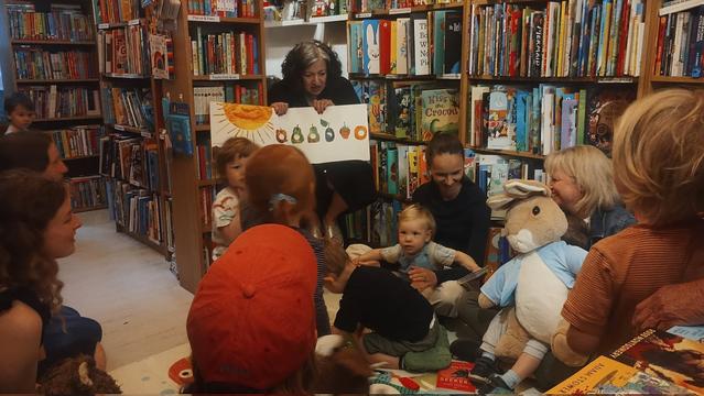 Bookseller Marie reading an oversized copy of The Very Hungry Caterpillar at the Edinburgh Bookshop's Under Fives Storytime, complete with a large, cuddly Peter Rabbit, who is getting some attention from the children!
