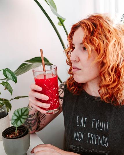 Woman about to drink a juice with a tank that says “eat fruit not friends”