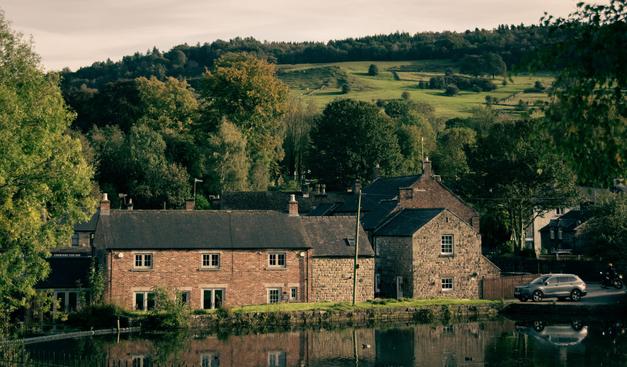 View across a pond of a old house against a hilly backdrop.  Mild evening sun.