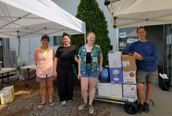 Group photo of 4 people on fruit sorting team, standing in front of a hand cart, loaded with boxes of sorted fruits. In front of the LifeCycles Victoria, office entrance.