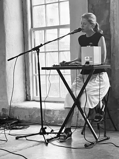 Black and white photo of woman singing and controlling electronics - with pouring rain visible through the window
