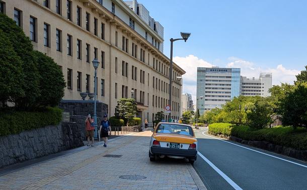 A Japanese taxi, photographed from the rear, parked fully on the sidewalk.
