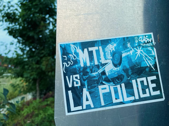 Blue-tinted photo of an upside down cop car with the words “MTL vs la police”—a sticker on a metal street sign