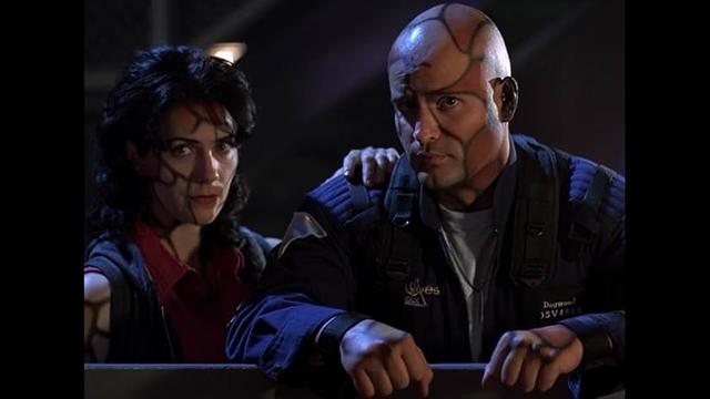 Holly Gagnier and Peter DeLuise as 2 genetically engineered or enhanced people from the SeaQuest series. They have Caucasian skin tone & darker brown as patches or patterns painted all over their skin, separated by 1 cm thick black lines. Slightly akin puzzle pieces, but not as jagged.

She has black hair and he's bald with big brown eyes. Both maybe in their late twenties. He's in a blue submarine uniform as a lieutenant in the Navy, she wears a red shirt under some blue vest style clothing.

The episode was Smoke on the Water.