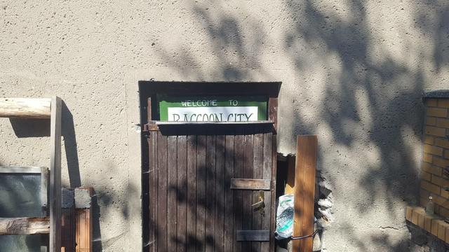 Eine alte Holztür in einem leicht verfallenen Steingemäuer.
Darauf ist noch ein Schild 'Racoon City' zu deutsch 'Waschbärstadt' erkennbar.

Hier haben früher unsere Waschbärbabys Waschabi & Watschilli gelebt, die wir ein Jahr als Ersatzeltern begleiten durften.

Heute ist da drin ein kleines Blockheizkraftwerk.