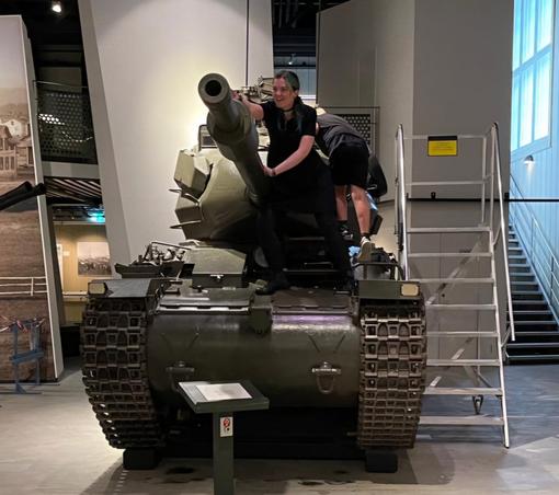 Jen on top of a tank, a kid in the background, busy looking inside the cockpit(?)