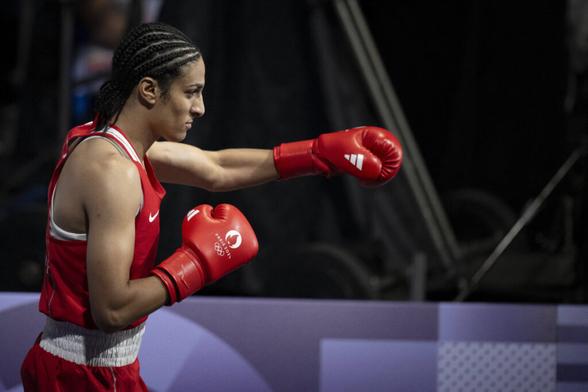 Die Boxerin Imane Khelif steht am linken Bildrand, sie trägt rote Boxkleidung und Handschuhe, den rechten Arm hat sie angewinkelt, den linken ausgestreckt. Ihr Haar ist zu Braids geflochten. Credit: