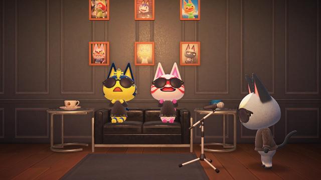 Animal Crossing: New Horizons screenshot. Image set in a black paneled wall room with hardwood flooring. A black couch has Ankha and Kabuki sitting wearing black sweaters and sunglasses while clapping. Raymond is next to them wearing the same in front of a mic while staring intensely. Next to each side of the couch is an end table with a coffee mug on it. On the wall in the back are photographs of various cat characters from Animal Crossing.