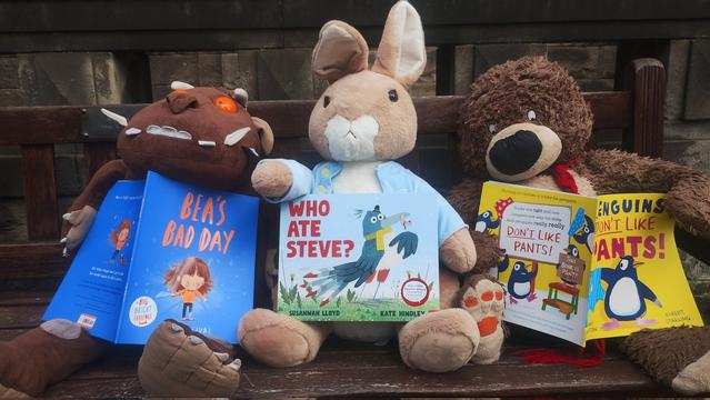Cuddly plushies of the children's book characters the Gruffalo, Peter Rabbit and Hugless Douglas reading different picture books on a bench outside the Edinburgh Bookshop