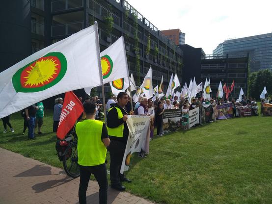 Wiese vor dem Landtag mit einer geschlossenen Reihe aus Menschen mit Transparenten und Fahnen der Jesiden.