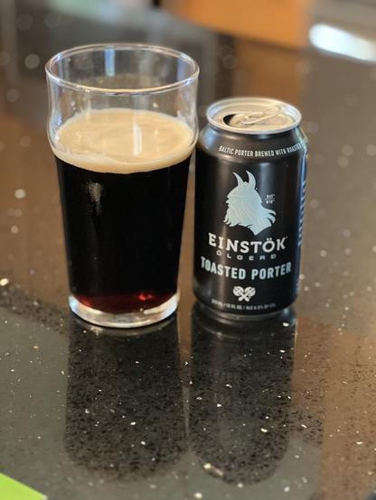 A pint glass of dark porter beer. The black can has a Viking in silhouette in light blue with white lettering and a pair of crossed battle axes.