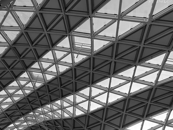 Geometric glass roof with a triangular lattice structure, creating an intricate pattern in a black and white photo.