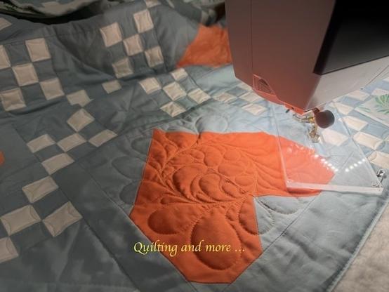 Detail of a pieced heart block in bright orange, quilted with free-flowing feathers on a blue-grey background.