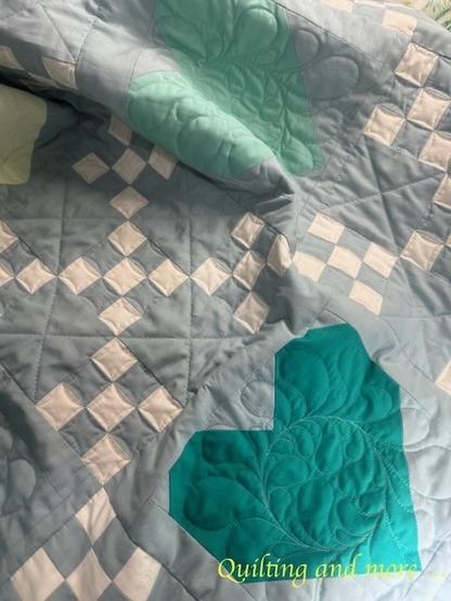Detail of a green heart block and a double nine-patch block in white and grey-blue. The nine-patch is quilted with small curves and straight lines.