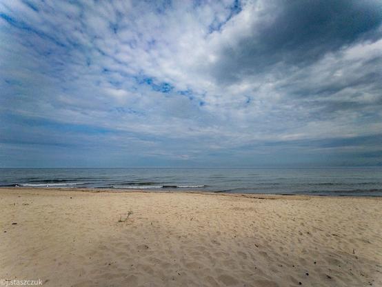Piaszczysta plaża prowadząca do spokojnego oceanu pod częściowo zachmurzonym niebem.