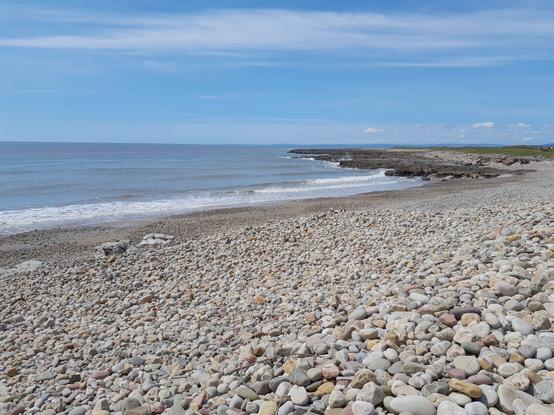 A pebble beach, bending right to a small headland, with incoming waves.