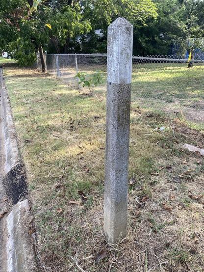 Concrete poll with white top (about the top 8-10”). It is square in shape with a pyramid top, sort of like a mini obelisk.