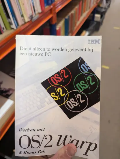 An OS/2 warp book held in front of the camera by a left hand.

The books text says "Only to be supplied with a new PC. 

Working with OS/2 Warp and Bonus pack"