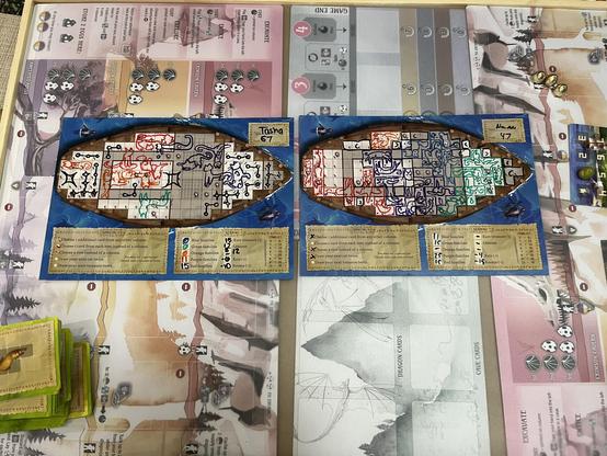 Two player boards from the game "The Isle of Cats," each with drawings of cats in different colors arranged within a ship grid. Cards and game components are present around the boards. Player scores are noted on each board.