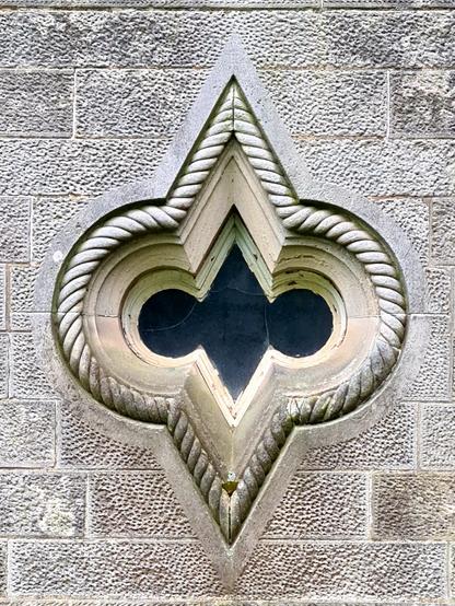 An unusually shaped window consisting of a diamond with two circles on either side which is surrounded by rope-like moulding.