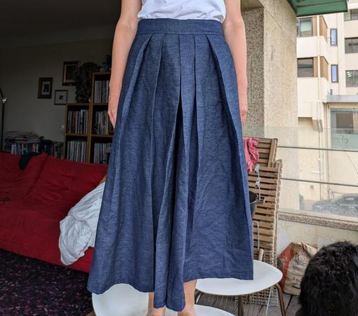 Woman stood on a white plastic chair, seen from the waist down, wearing a pair of hakama - trousers with 6 pleats in the front (and 2 in the back) - in blue denim, with very, very wide bottoms