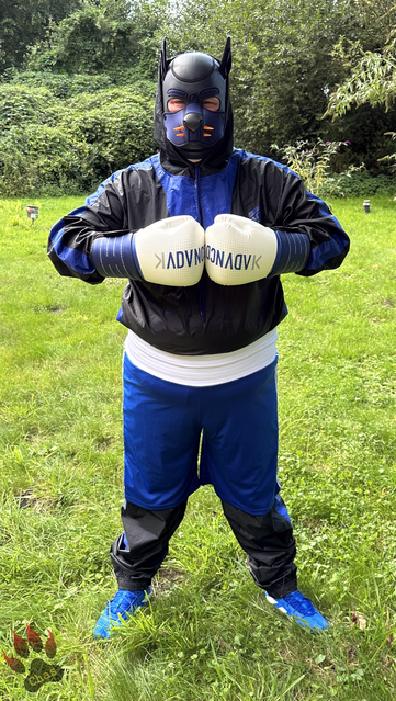 human pup in sweatsuit and boxing gear (boots, trunks and gloves) standing outside in the garden, both hands put together in front of chest